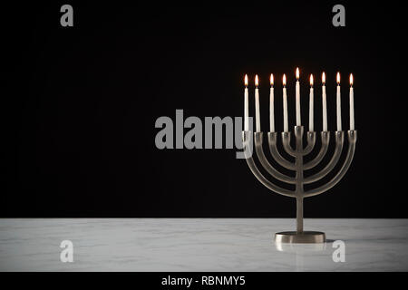 Kerzen auf Metall Hanukkah Menorah auf Marmor Oberfläche gegen Schwarz Studio Hintergrund Stockfoto
