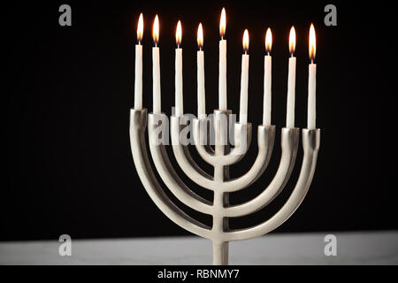 Kerzen auf Metall Hanukkah Menorah auf Marmor Oberfläche gegen Schwarz Studio Hintergrund Stockfoto