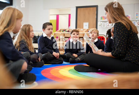 Weibliche Lehrer sitzen auf dem Boden in einem Klassenzimmer mit einem Buch zu ihrer Klasse, selektiven Fokus Stockfoto