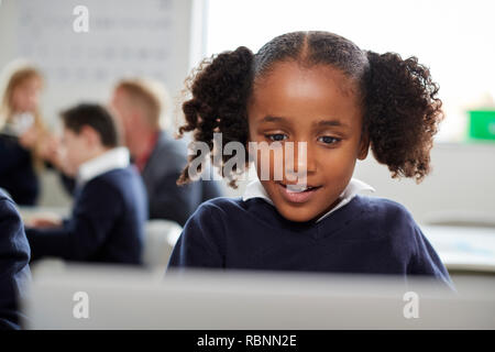 Junge schwarze Schülerin mit einem Laptop auf dem Schreibtisch in einer Grundschule im Klassenzimmer sitzen, vorne, Stockfoto