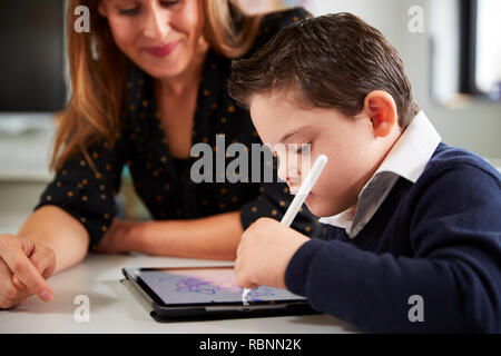 Nahaufnahme von jungen weiblichen Lehrer am Schreibtisch mit Down Syndrom mit einem Tablet Computer Schüler in einer Grundschule Klassenzimmer sitzend, Nahaufnahme, Seitenansicht Stockfoto