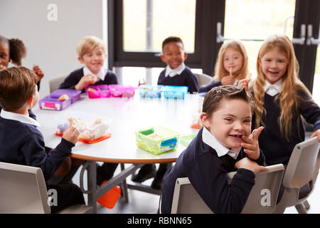 Ansicht der Grundschule Kinder sitzen gemeinsam an einem runden Tisch ihre Lunchpakete zu Essen, einige Drehen um die Kamera Stockfoto