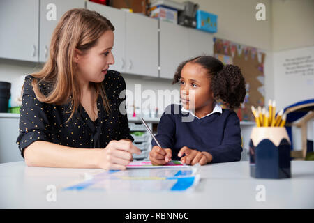 Junge weibliche Grundschullehrerin arbeitet auf einer mit einer Schülerin an einem Tisch in einem Klassenzimmer, an einander suchen, Nahaufnahme Stockfoto