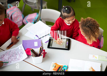 Aussicht auf zwei Infant school Mädchen an einem Tisch sitzen erhöht, mit einem Tablet Computer und Stylus in einem Klassenzimmer Stockfoto