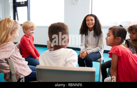 Eine Klasse für Kleinkinder Schulkinder sitzen auf Stühlen im Kreis im Klassenzimmer sprechen mit ihrer Lehrerin Stockfoto