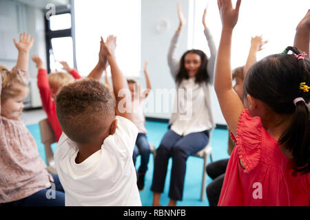 Eine Klasse für Kleinkinder Schulkinder sitzen auf Stühlen im Kreis im Klassenzimmer, heben die Hände mit ihrer Lehrerin, in der Nähe Stockfoto