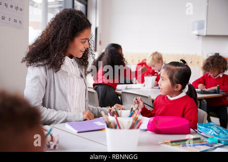 Weibliche Kindergärtnerin am Tisch in einem Klassenzimmer sitzen mit einem jungen chinesischen Schoolgirl, Nahaufnahme Stockfoto