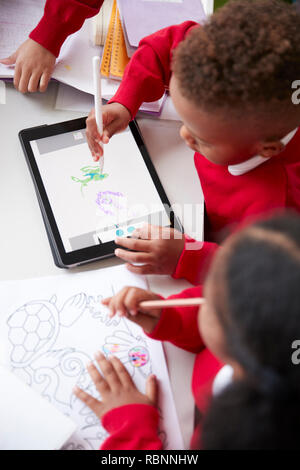 Ansicht von zwei Kindergarten Kinder an einem Schreibtisch in einem Klassenzimmer Zeichnung mit einem Tablet-PC und Stylus sitzend, Nahaufnahme, vertikal Stockfoto
