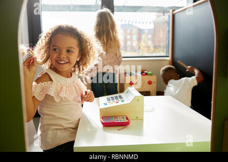 Zwei junge Mädchen und ein Junge, die zusammen spielen in einem Spielhaus an Infant School, Hintergrundbeleuchtung Stockfoto