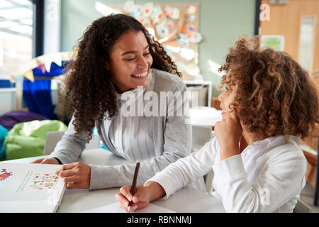 Weibliche Infant School Lehrer arbeitet auf einer mit einer jungen Schülerin, sitzen an einem Tisch in jeder anderen, Vorderansicht, Lächeln, Nahaufnahme Stockfoto
