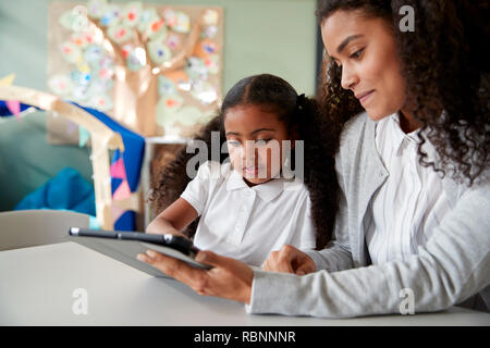 Nahaufnahme eines jungen schwarzen Schülerin an einem Tisch sitzen in einem Kind Schule Unterricht lernen auf einem mit einer Lehrerin über einen Tablet-PC, in der Nähe Stockfoto