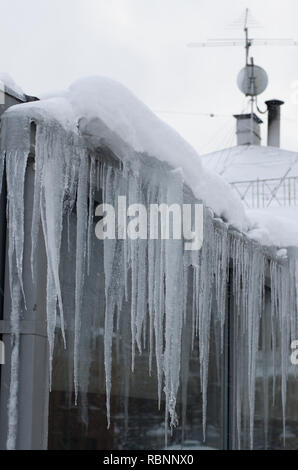 Lange Eiszapfen hängen von dem Dach des Hauses an einem bewölkten Tag im Winter Stockfoto