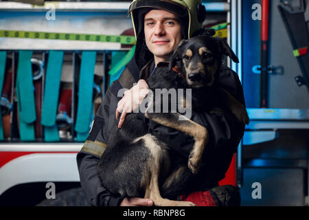 Image der jungen Feuerwehrmann in Helm mit Hund auf dem Hintergrund der fire truck Stockfoto