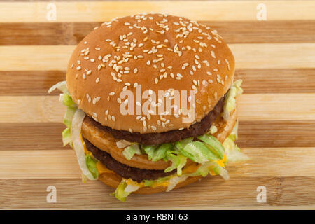 In der Nähe Bild von köstlichen doppelten Cheeseburger mit Rindfleisch, Cheddar und Salat in einem sesambrötchen. Ansicht von oben. Holz- Hintergrund Stockfoto