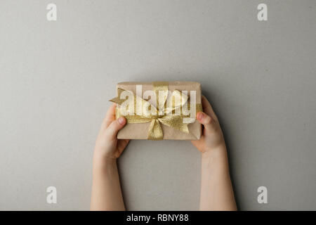 Handwerk Geschenkkarton mit Gold Bug in der Kinder Hände auf grauem Hintergrund, Einkaufen, Verkauf, Muttertag, Valentinstag, Weihnachten Konzept kopieren Raum, flach Stockfoto