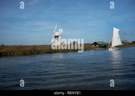 Eine gebrochene Sloop Segelboot, eine Windmühle auf dem Fluss Thurne, die auf einem klaren Herbstmorgen, Norfolk Broads, Norfolk, England, Großbritannien Stockfoto