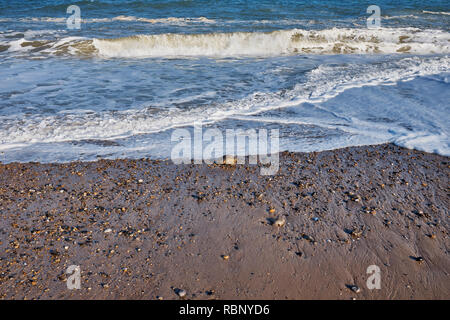 Eine Nahaufnahme von einem Strand mit Sand, Kiesel und Steine mit Wellen auf den Strand brechen als die Flut beginnt in zu kommen, England, Großbritannien Stockfoto
