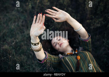 Schöne boho Mädchen auf Gras mit Händen liegen. Fokus auf der Hand Stockfoto