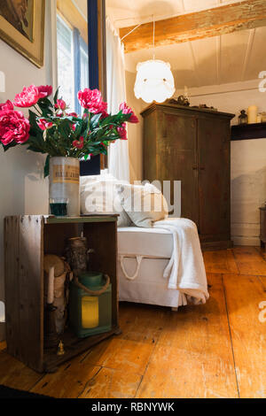 Alte Holzkiste Tabelle, mit rosa Seide Blumen in der Vase, armlose weiß gepolsterten Stuhl und antiken Holzwandschrank im Wohnzimmer in alten 1862 Home Stockfoto