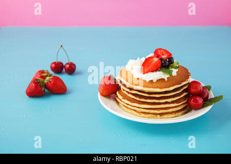 Pfannkuchen in einer Platte mit Sahne, Erdbeeren, Minze und Süßkirschen auf einem hellen Blau und Rosa Hintergrund. Platz kopieren Stockfoto
