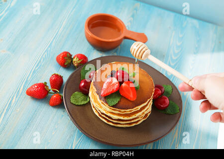 Pfannkuchen in einem Teller mit Erdbeeren, Minze, Honig und Kirsche auf einer hellen blauen Hintergrund. Platz kopieren Stockfoto
