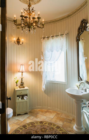 Weißes Porzellan-Sockelwaschbecken, Toilette, kleiner Holzschrank und Lampe im Gästebad in einem Haus im Renaissance-Stil. Stockfoto