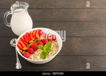 Gesundes Frühstück mit Müsli, Himbeeren, Erdbeeren, Mandeln und Milch auf Holztisch mit Kopie Raum Stockfoto