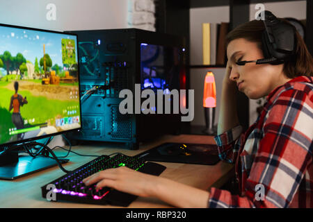 Porträt einer jungen Frau mit Kopfhörern am Tisch sitzen, spielen, Computer online spiele Stockfoto