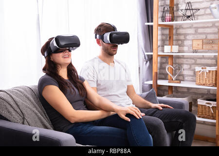 Junges Paar sitzt auf einem Sofa mit Virtual Reality Headset Stockfoto