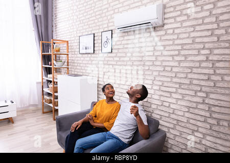 Junge afrikanische Paar auf dem Sofa, die Klimaanlage zu Hause sitzen Stockfoto