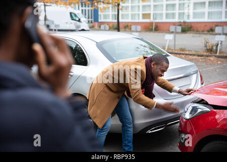 Frau ruft um Hilfe Vor Mann Inspektion beschädigt Auto auf der Straße Stockfoto