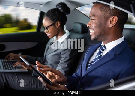 Zwei glückliche Afrikanische Geschäftsleute mit elektronischen Geräten bei Anreise mit dem Auto Stockfoto