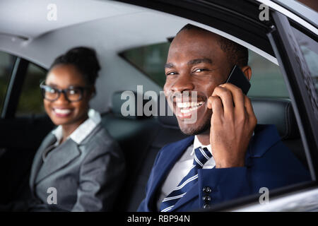 Gerne Unternehmer Sitzen im Auto neben seiner Kollegin Gespräch am Handy Stockfoto
