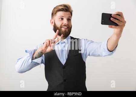 Bild von ein hübscher junger bärtiger Mann stehend über weiße Wand Hintergrund nehmen ein selfie per Handy. Stockfoto