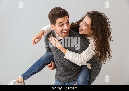 Bild von freudiges Paar Spaß und während Mann huckepack attraktive Frau über grauer Hintergrund Stockfoto