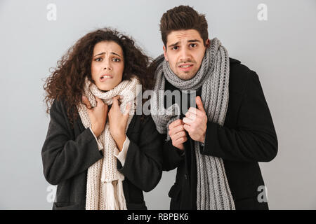 Gefrorene junges Paar tragen Pullover und Schals stehen über grauen Hintergrund isoliert, Frösteln Stockfoto
