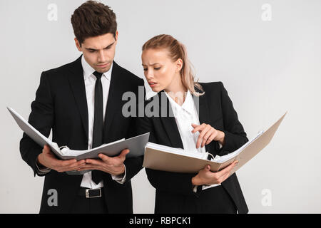 Selbstbewussten jungen Geschäft Paar stehend über grauen Hintergrund isoliert, durch Dokumente Stockfoto