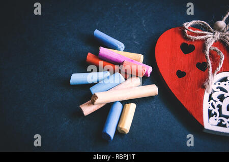 Handgefertigte rotes Herz close-up und Stücke von pastellkreideblöckchen auf dunklem Hintergrund, Symbol der Liebe, Happy Valentine's Day. Stockfoto