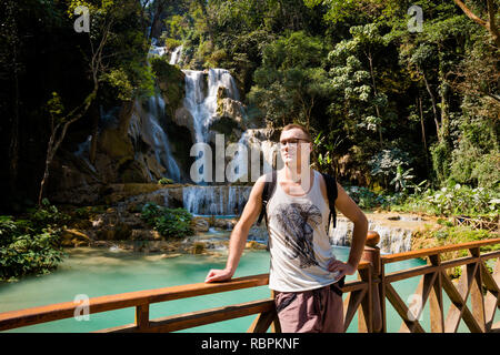 Jungen kaukasischen Mann auf erstaunliche Kuang Si Wasserfall in der Nähe von touristischen Luang Prabang in Laos. Alte Holzbrücke und Landschaft der Natur in Südostasien d Stockfoto