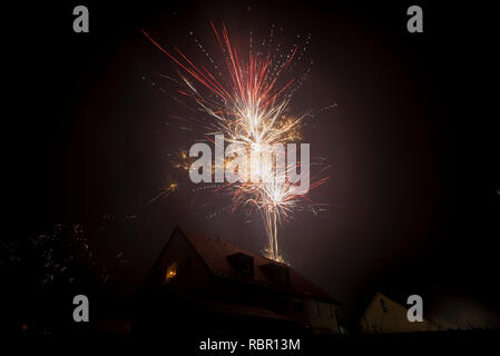 Mann mit Wunderkerzen im Fenster eines Wohnhauses wir das Feuerwerk Aufhellung des Nachthimmels zu Neujahr Stockfoto