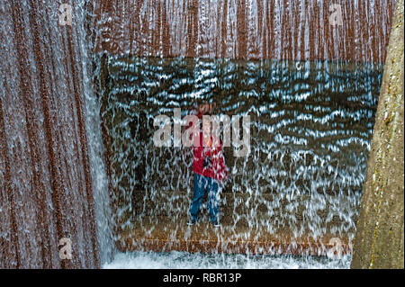 Ein kleiner Junge steht hinter einem plätschernden Springbrunnen in der Stadt Portland, Oregon Stockfoto