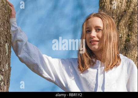 Nahaufnahme von einem jungen Mädchen, das in einem Baum mit braunen Haaren lächelnd und mit Blick auf die Kamera Stockfoto