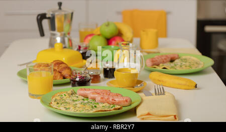 Zeit für das Frühstück. Omelette mit grünen und Würstchen. Orangensaft, Croissants und Marmelade. Kaffee mit Sahne oder Milch. Früchte wie Bananen, rote und grüne Äpfel. Stockfoto