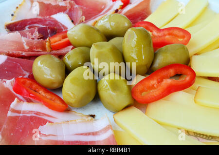 Vorspeise, grüne Oliven mit in Scheiben geschnittenen Schinken, geräucherter Ziegenkäse und ein paar Stücke von Red Hot peppers auf rustikalen, Keramik Teller serviert Stockfoto