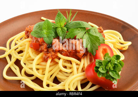 Spaghetti Bollognese mit frischen Kräuter Gewürze - Oregano, Basilikum, Rosmarin, Sellerie und Paprika, auf rustikalen, braun Keramik Platte über weiße serviert. Stockfoto