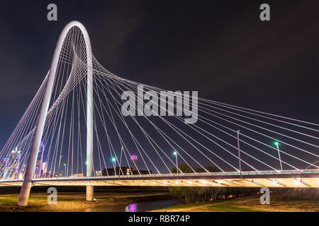 Die ikonischen Margaret Hunt Hill Suspension Bridge bei Nacht, mit Blick auf die hellen Lichter der Dallas, Texas, Skyline im Hintergrund. Stockfoto