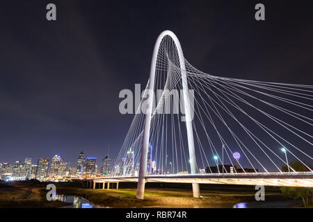 Die ikonischen Margaret Hunt Hill Suspension Bridge bei Nacht, mit Blick auf die hellen Lichter der Dallas, Texas, Skyline im Hintergrund. Stockfoto