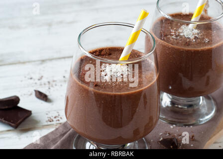 Schokolade Banane Smoothie oder Milchshake mit Kokosnuss auf weissem Holztisch. Stockfoto