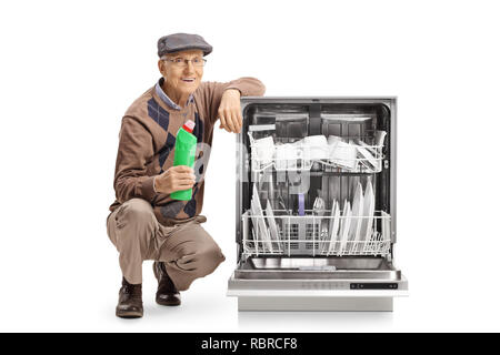 Älterer Mann mit Spülmittel und kniete neben einem Geschirrspüler auf weißem Hintergrund Stockfoto