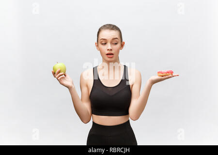 Junge Frau die Wahl zwischen Donut und Apple auf weißem Hintergrund. Ernährung Lebensmittel Konzept Stockfoto